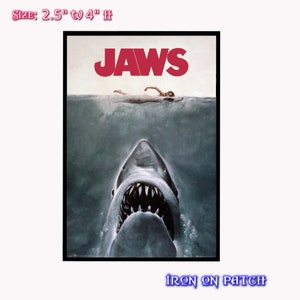 May include: Iron-on patch featuring the Jaws movie poster. The patch shows a close-up of the shark's mouth with the word "JAWS" in red letters above the shark. The patch is 2.5 inches wide and 4 inches tall.