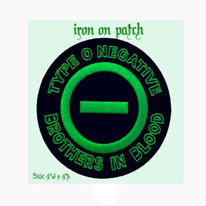 May include: Green and black iron-on patch with the text "Type O Negative Brothers in Blood" in a circle around a green negative symbol. The patch is 10 cm wide and 10 cm high.