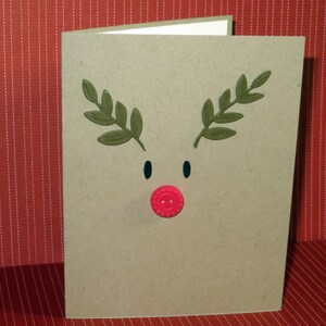 May include: A brown card with a reindeer face made from green paper leaves and a red button nose.