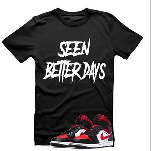 May include: Black t-shirt with white text that reads "SEEN BETTER DAYS" in a graffiti style font. A pair of black, red, and white sneakers are in the bottom of the image.