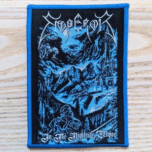 Pode incluir: Patch bordado com fundo preto e borda azul. O patch apresenta a palavra "Emperor" em uma fonte estilizada na parte superior, com um design de paisagem azul e preto abaixo. O texto "In The Nightside Eclipse" está na parte inferior.