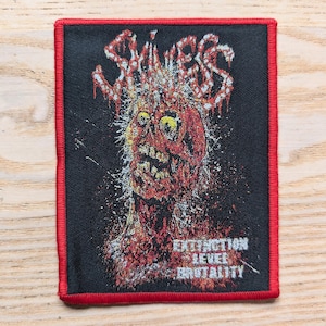 May include: A black patch with a red border featuring a graphic of a zombie-like figure with the word "SKINESS" in red dripping letters. The text "EXTINCTION LEVEL BRUTALITY" is below the graphic.