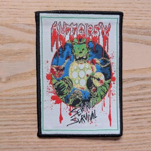 Op de afbeelding: Rechthoekige patch met een zwarte rand. De patch heeft het woord "Autopsy" in rode, druipende letters. De centrale afbeelding is van een groen wezen met een blauwe en gele achtergrond, en de woorden "Severed Survival" in het wit.