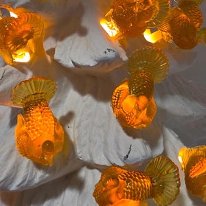 May include: A string of amber-colored, translucent turkey-shaped light covers arranged on a white, textured, tree-shaped base. Each turkey figure features detailed feather textures and glows from within, creating a warm, illuminated display.