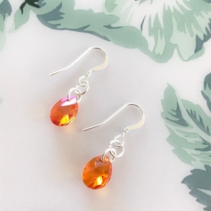 May include: A pair of silver dangle earrings with teardrop-shaped orange and pink iridescent crystals.