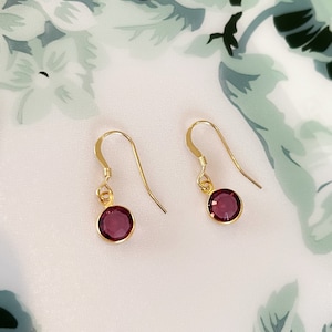 May include: A pair of gold dangle earrings with small, round, dark purple gemstones.