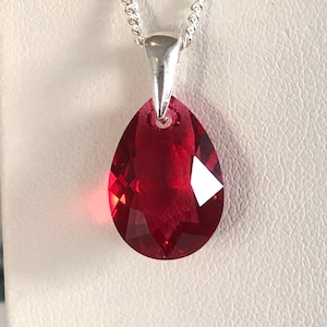 May include: A faceted, red crystal pendant in a teardrop shape suspended from a silver chain. The pendant's deep ruby hue catches the light, producing a sparkling effect. The delicate silver chain enhances the pendant's brilliance.