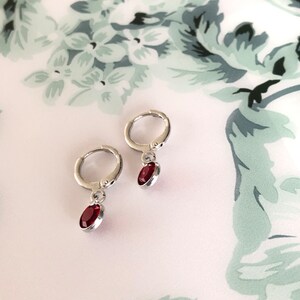 May include: A pair of silver hoop earrings with a dangling red gemstone. The earrings are small and delicate.