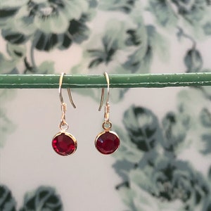 May include: A pair of silver dangle earrings with small, round, red gemstones.