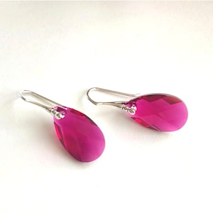 May include: A pair of silver dangle earrings with teardrop-shaped pink crystal stones.