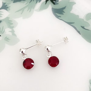 May include: A pair of silver dangle earrings with a small red crystal hanging from each earring.