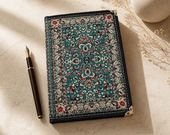 Puede incluir: Un cuaderno rectangular con un patrón floral en verde azulado, rojo y crema que recuerda a una alfombra, con bordes negros y protectores de esquina de metal dorado. Una pluma estilográfica negra con detalles dorados se sitúa a la izquierda.
