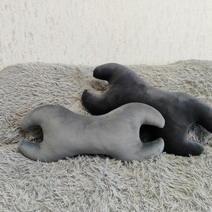 May include: Two gray and black lumbar support pillows shaped like a wrench. The pillows are on a fluffy gray rug.