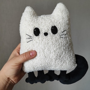 May include: White plush cat toy with black embroidered eyes, whiskers, and paws. The cat has a fluffy white body and a black tail.