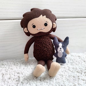 Puede incluir: Un juguete de peluche marrón con un cuerpo peludo marrón y una cara sonriente. El juguete tiene un pequeño perro de peluche gris en sus brazos.