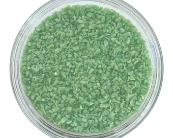 Puede incluir: Un tarro de cristal transparente lleno de pequeños trozos verde claro de forma irregular. Los trozos parecen ser una sustancia granular, posiblemente material decorativo o artesanal. El tarro es redondo y está sobre un fondo blanco.