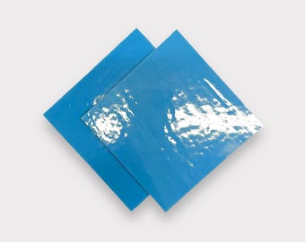 May include: Two square tiles with a glossy, blue glaze. The glaze has a rippled, textured surface.