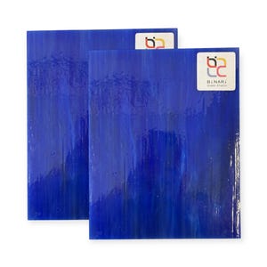 May include: Two sheets of vibrant blue stained glass with a textured, flowing pattern. Each sheet has a glossy finish and a small white label with the text "Binari Glass Studio" and a logo. The glass has a rich, deep color.