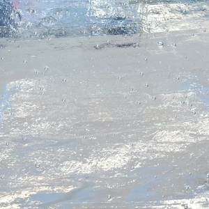 May include: A close-up of a light blue, textured glass surface with small air bubbles throughout. The surface has a subtle shimmer and reflects light.