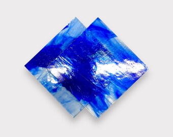 May include: Two overlapping squares of blue glass with white swirls and streaks. The glass is translucent and reflects light.