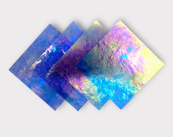 May include: Four iridescent squares of glass, layered on top of each other. The squares are in shades of blue, purple, and yellow.