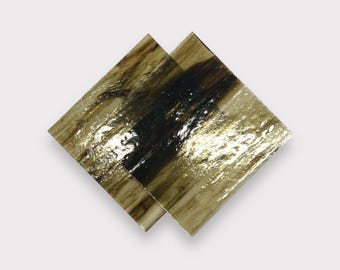 May include: Two square pieces of glass with a wood grain pattern and gold leaf accents. The glass is translucent and has a dark brown and gold color.