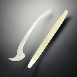 May include: Two white plastic tools for applying glue or adhesive. One tool is a curved scraper with a pointed tip. The other tool is a flat scraper with a rounded tip.