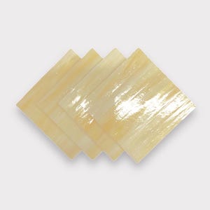 May include: Four square, translucent, pale yellow glass tiles with a subtle, iridescent sheen. The tiles are stacked on top of each other, creating a layered effect.