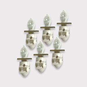 Puede incluir: Seis bombillas de luz nocturna blancas con bases de metal plateado y bombillas de vidrio transparente. Las bombillas están dispuestas en semicírculo sobre un fondo blanco.