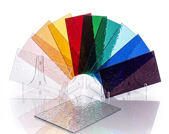 May include: A collection of rectangular, textured glass sheets arranged in a fan shape, featuring a spectrum of colors including clear, pink, orange, yellow, red, dark red, green, teal, blue, and purple, with one clear sheet lying flat in front.