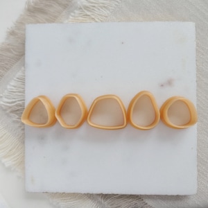 Könnte beinhalten: Fünf kleine, hellbraune, geometrische Formen aus Keramik, die in einer Reihe auf einer weißen Oberfläche angeordnet sind. Die Formen sind alle leicht unterschiedlich, aber sie sind alle in Größe und Form ähnlich.