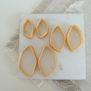 Może przedstawiać: Sześć beżowych plastikowych foremek do ciasteczek w kształcie zaokrąglonego diamentu, ułożonych na białym marmurowym blacie.