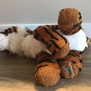 May include: A plush tiger toy with brown and black stripes, white fur on the face and chest, and a blue tag on the foot that says "Animal Planet".