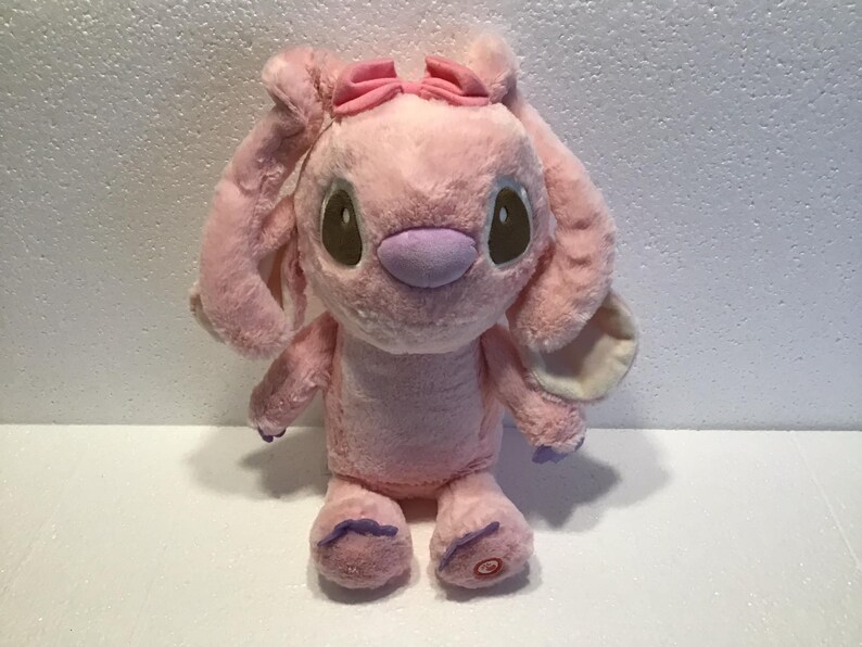 May include: Pink plush toy with large ears, a pink bow, and purple accents. The toy has brown eyes and a stitched smile.