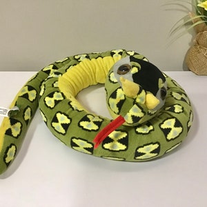 May include: Green and yellow plush snake toy with a black and white pattern. The snake is curled up in a circle with its head facing the camera. The snake has a red tongue.