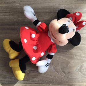 May include: A red and white polka dot dress with a black bow on top of the head. The plush toy is a cartoon character with black ears and a black nose.