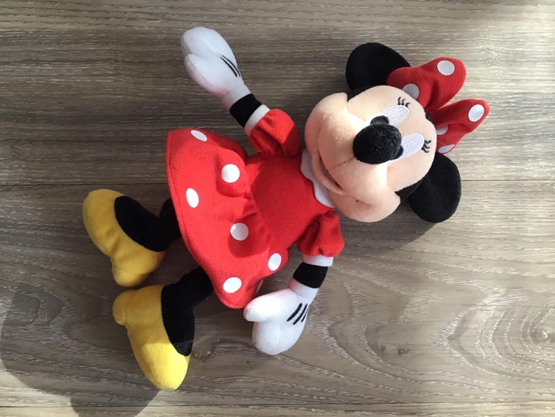 May include: A red and white polka dot dress with a black bow on top of the head. The plush toy is a cartoon character with black ears and a black nose.