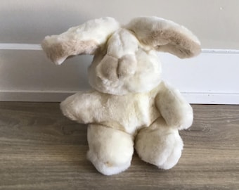 May include: A white plush bunny with brown ears. The bunny is sitting on a wooden floor.