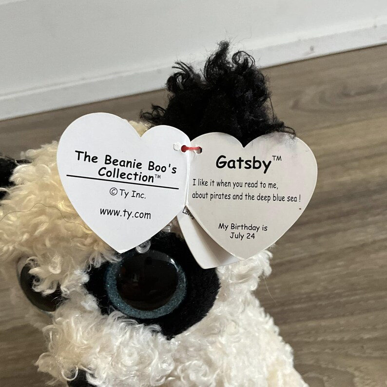 May include: White and black plush toy with a heart-shaped tag that reads "The Beanie Boo's Collection" and "Gatsby". The tag also includes the text "I like it when you read to me, about pirates and the deep blue sea!" and "My Birthday is July 24".