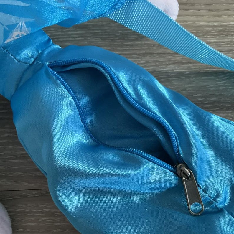May include: A close-up of a light blue satin bag with a zipper closure. The bag has a matching blue strap and a white fluffy accent. The zipper is silver in color.