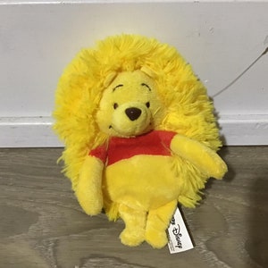 May include: A yellow plush Winnie the Pooh lion with a red shirt. The plush toy has a tag that says "Disney".