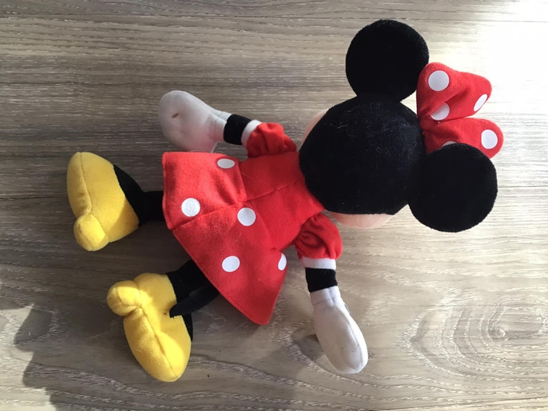 May include: A red and white polka dot plush toy of Minnie Mouse with black ears and a red bow with white polka dots.