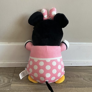 K&ouml;nnte beinhalten: Ein Pl&uuml;schtier einer Comicmaus mit schwarzen Ohren und einem rosa Kleid mit wei&szlig;en Punkten. Die Maus tr&auml;gt eine schwarze Schleife mit wei&szlig;en Punkten auf dem Kopf. Das Spielzeug hat gelbe F&uuml;&szlig;e und einen schwarzen Schwanz.