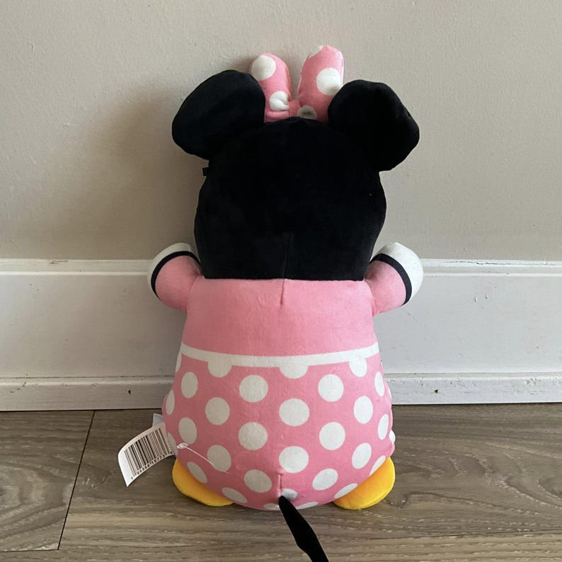 K&ouml;nnte beinhalten: Ein Pl&uuml;schtier einer Comicmaus mit schwarzen Ohren und einem rosa Kleid mit wei&szlig;en Punkten. Die Maus tr&auml;gt eine schwarze Schleife mit wei&szlig;en Punkten auf dem Kopf. Das Spielzeug hat gelbe F&uuml;&szlig;e und einen schwarzen Schwanz.
