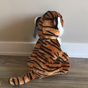 May include: A plush tiger toy with orange and black stripes. The toy is sitting on a wooden floor.