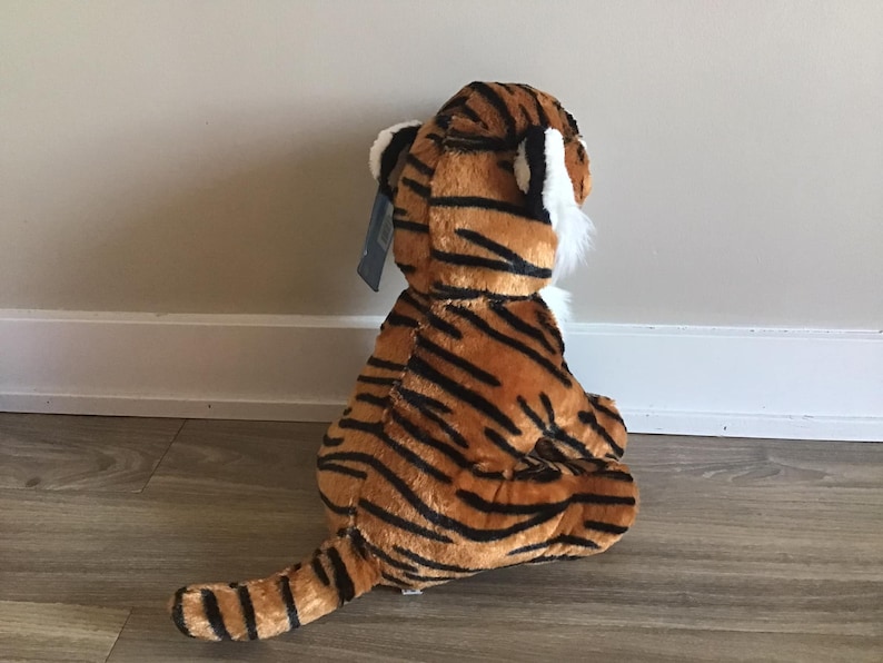 May include: A plush tiger toy with orange and black stripes. The toy is sitting on a wooden floor.