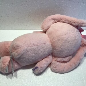 May include: A pink plush bunny with long ears and a white tag attached to its leg. The bunny is lying on its side with its head resting on its arm.