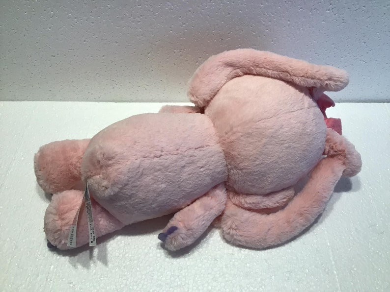 May include: A pink plush bunny with long ears and a white tag attached to its leg. The bunny is lying on its side with its head resting on its arm.