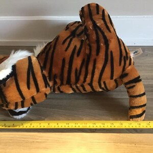 May include: A plush tiger toy with orange and black stripes. The toy is lying on its belly with its head turned to the side. The toy is about 18 inches long.