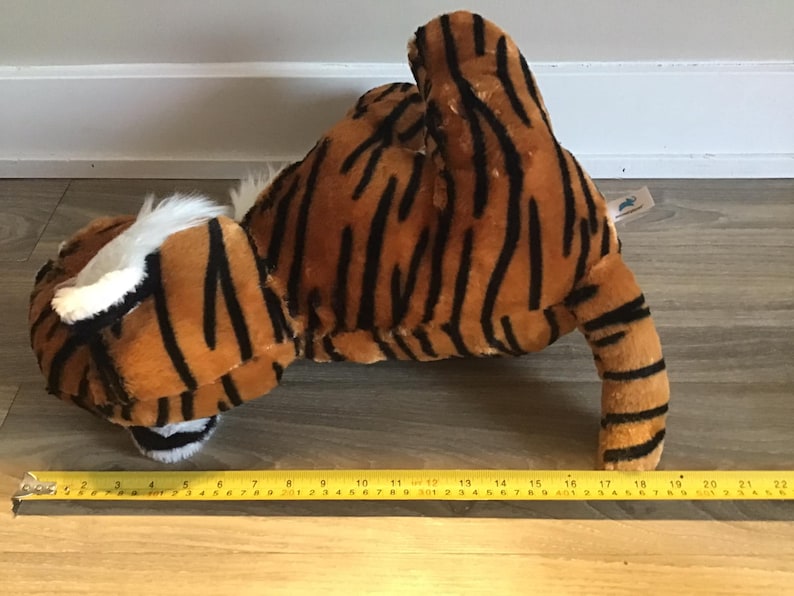May include: A plush tiger toy with orange and black stripes. The toy is lying on its belly with its head turned to the side. The toy is about 18 inches long.